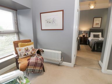 A corner with a leather chair with cushions and a blanket next to a window and a radiator overlooking a bedroom with two single beds Dale Cottage Llanrwst