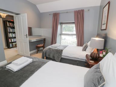 A bedroom with two beds a bedside table with a lamp a window with curtains and a small desk with a chair at Dale Cottage in Llanrwst