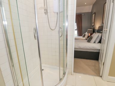 A bathroom shower with glass doors opening to a bedroom with two beds and a lamp at Dale Cottage in Llanrwst