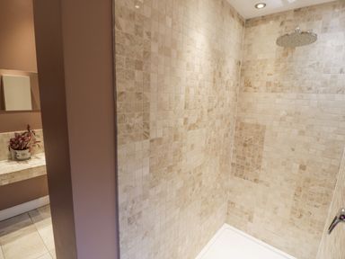 A shower area with beige tiled walls and a round showerhead at Dale Cottage in Llanrwst