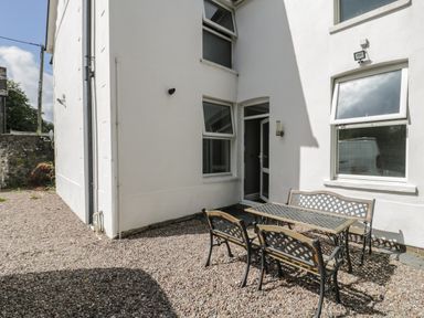 An outdoor patio area with a metal table and benches on gravel outside a white building at Dale Cottage in Llanrwst
