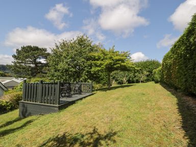 A garden with a raised wooden deck and metal chairs and tables surrounded by trees and hedges at Dale Cottage in Llanrwst