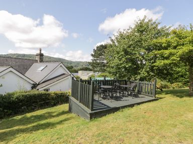 A garden with a raised wooden deck and metal chairs and tables at Dale Cottage in Llanrwst