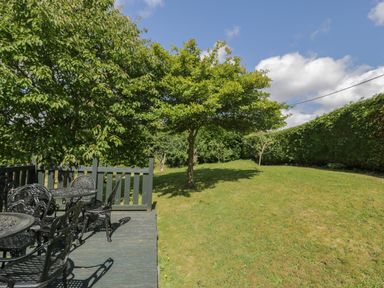 A garden with a wooden deck and metal chairs and tables and trees at Dale Cottage in Llanrwst