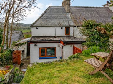 The rear view of a two storey house with a stone slate roof and garden with wooden outdoor furniture at Pen Y Graig in Talysarn