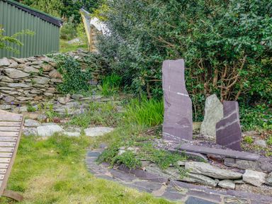 An outdoor garden area with stone sculptures stone wall plants and grass at Pen Y Graig in Talysarn