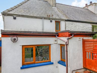 The exterior of a house with white walls blue window sills and brown framed windows at Pen Y Graig in Talysarn