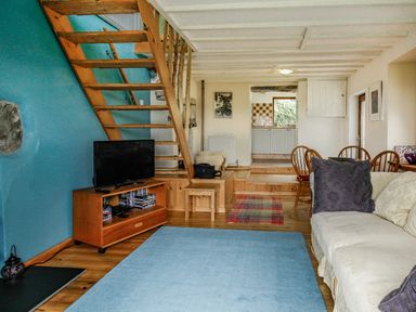 A living room with wooden stairs a television a sofa and a dining area at Pen Y Graig in Talysarn