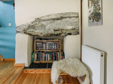 A built in bookshelf in a fireplace with books and dvds a wooden floor a small chair with a white fluffy cover a radiator and a blue wall at Pen Y Graig in Talysarn