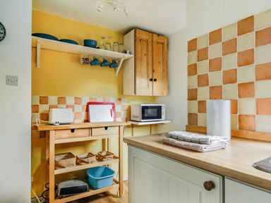 A kitchen with wooden cabinets a microwave cutting boards open shelf with dishes and mugs and counter with towels and paper towel at Pen Y Graig in Talysarn