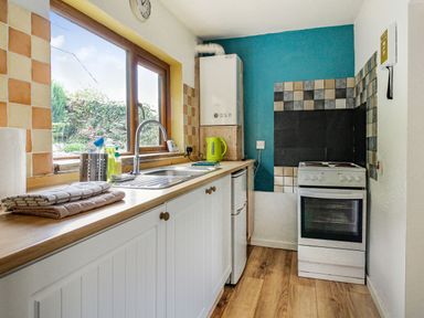 A kitchen with a sink under a window a stove and a kettle on the counter at Pen Y Graig in Talysarn