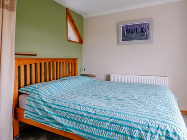 A bedroom with a wooden bed frame and a teal patterned bedspread at Pen Y Graig in Talysarn