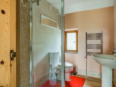 A bathroom with a shower, toilet, sink, towel radiator, window, and a red rug at Pen Y Graig in Talysarn