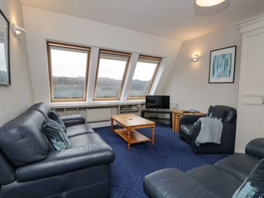 A living room with leather sofas a wooden coffee table and slanted windows at Rothay 17 in Ambleside