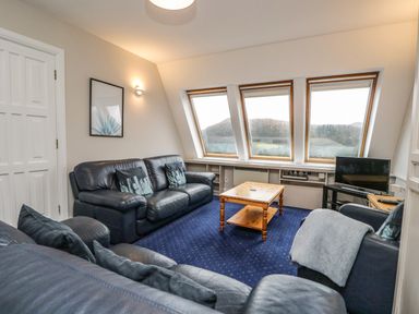 A living room with leather sofas wooden table and windows overlooking hills at Rothay 17 in Ambleside