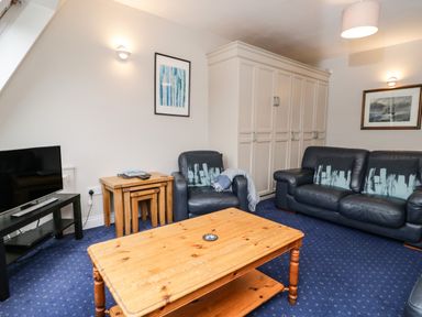 A living room with black leather sofas, wooden coffee table, TV on a black stand, nested side tables, and framed artwork on the walls at Rothay 17 in Ambleside
