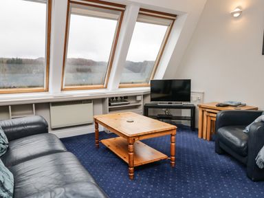 A sitting room with leather sofas a wooden coffee table a TV and slanted windows at Rothay 17 in Ambleside