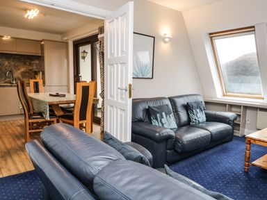 A living room with blue leather sofas and a wooden dining table in an open kitchen area at Rothay 17 in Ambleside