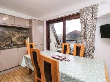A dining area with a table and chairs next to a kitchen and a glass door leading to a balcony at Rothay 17 in Ambleside