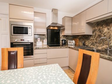 A kitchen with built in microwave oven kettle toaster sink and wooden chairs at Rothay 17 in Ambleside