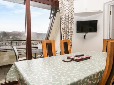 A dining table with chairs near a glass door leading to a balcony and a wall-mounted television at Rothay 17 in Ambleside