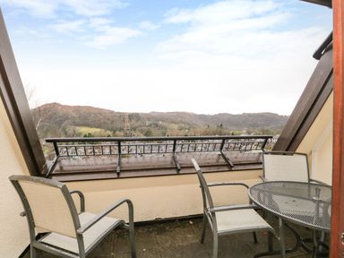 A balcony with two chairs and a round metal table overlooking hills and rooftops at Rothay 17 in Ambleside