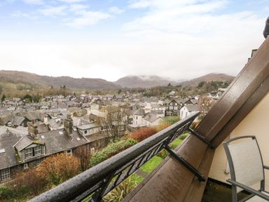 A balcony with a chair overlooking rooftops and hills in the distance at Rothay 17 in Ambleside