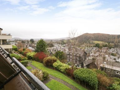 A view of a town with houses trees and hills from a balcony with a railing at Rothay 17 in Ambleside