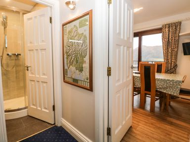 A hallway with open doors leading to a bathroom with a shower and a dining area with a table and chairs at Rothay 17 Ambleside