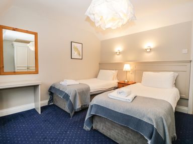 A bedroom with two single beds with gray blankets and white linens a wooden nightstand with a lamp a wall mirror and a framed picture at Rothay 17 in Ambleside