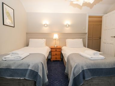 A bedroom with two single beds a wooden nightstand with a lamp between them and a framed picture on the wall at Rothay 17 in Ambleside
