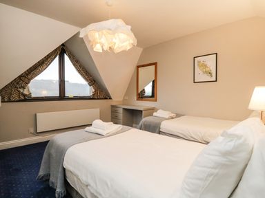 A bedroom with two single beds a triangular window and a desk with a mirror at Rothay 17 in Ambleside