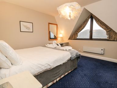 A bedroom with a double bed a side table with lamp a mirror a framed picture and triangular window with curtains at Rothay 17 Ambleside
