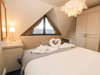 A bedroom with a bed featuring towel swans on a gray throw blanket near a triangular window with patterned curtains at Rothay 17 in Ambleside