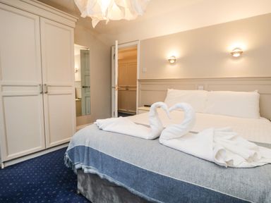 A bedroom with a bed with towel swans on it a wardrobe and an open door at Rothay 17 in Ambleside