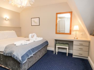 A bedroom with a bed, a desk with drawers, a mirror, a lamp, and a stool at Rothay 17 in Ambleside