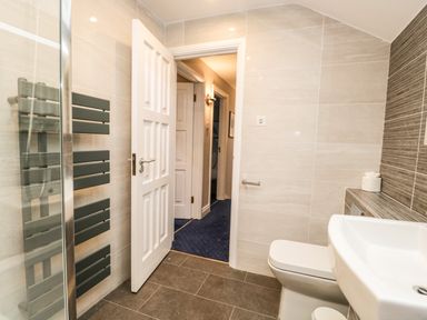 A bathroom with a white door open to a hallway with blue carpet at Rothay 17 in Ambleside