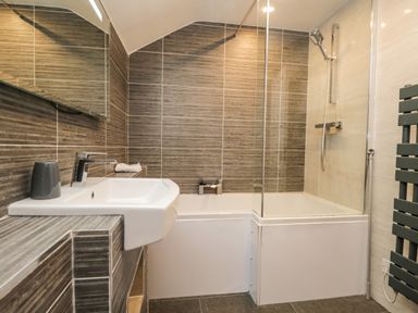 A bathroom with a bathtub shower combination a sink a wall-mounted mirror and a heated towel rail at Rothay 17 in Ambleside