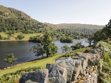 A lake surrounded by hills and trees with a stone wall in the foreground at Rothay 17 in Ambleside