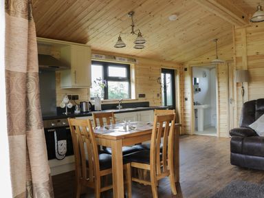 A kitchen and dining area with wooden table and chairs near window and a brown leather sofa at Hayfields in Grimston