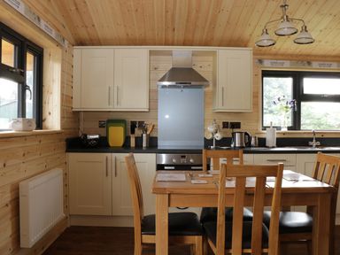 A kitchen with wooden dining table and chairs cabinets stove kettle and windows at Hayfields in Grimston