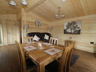 A dining area with a wooden table and chairs next to a living room with a sofa and wall clock at Hayfields in Grimston