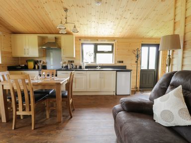 A wooden kitchen with dining table and chairs next to a brown sofa at Hayfields in Grimston