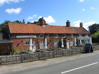 A brick building with a tiled roof and outdoor seating behind a wooden fence at The Three Horseshoes