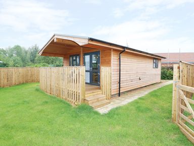 A small wooden house with a fenced front yard and a stone pathway at Hayfields in Grimston