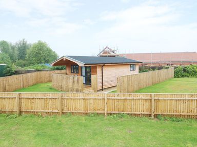 A small wooden house with a fenced yard and grass at Hayfields in Grimston