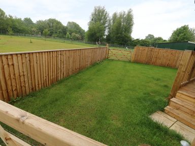 A fenced grass backyard with a wooden gate and steps leading to the lawn at Hayfields in Grimston