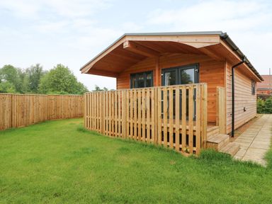 A wooden cabin with a fenced porch and a grassy yard at Hayfields in Grimston