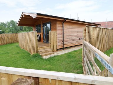 A wooden cabin with a covered porch and fenced yard at Hayfields in Grimston