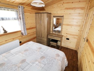 A bedroom with a bed, wardrobe, dressing table, and window with curtains at Hayfields in Grimston
